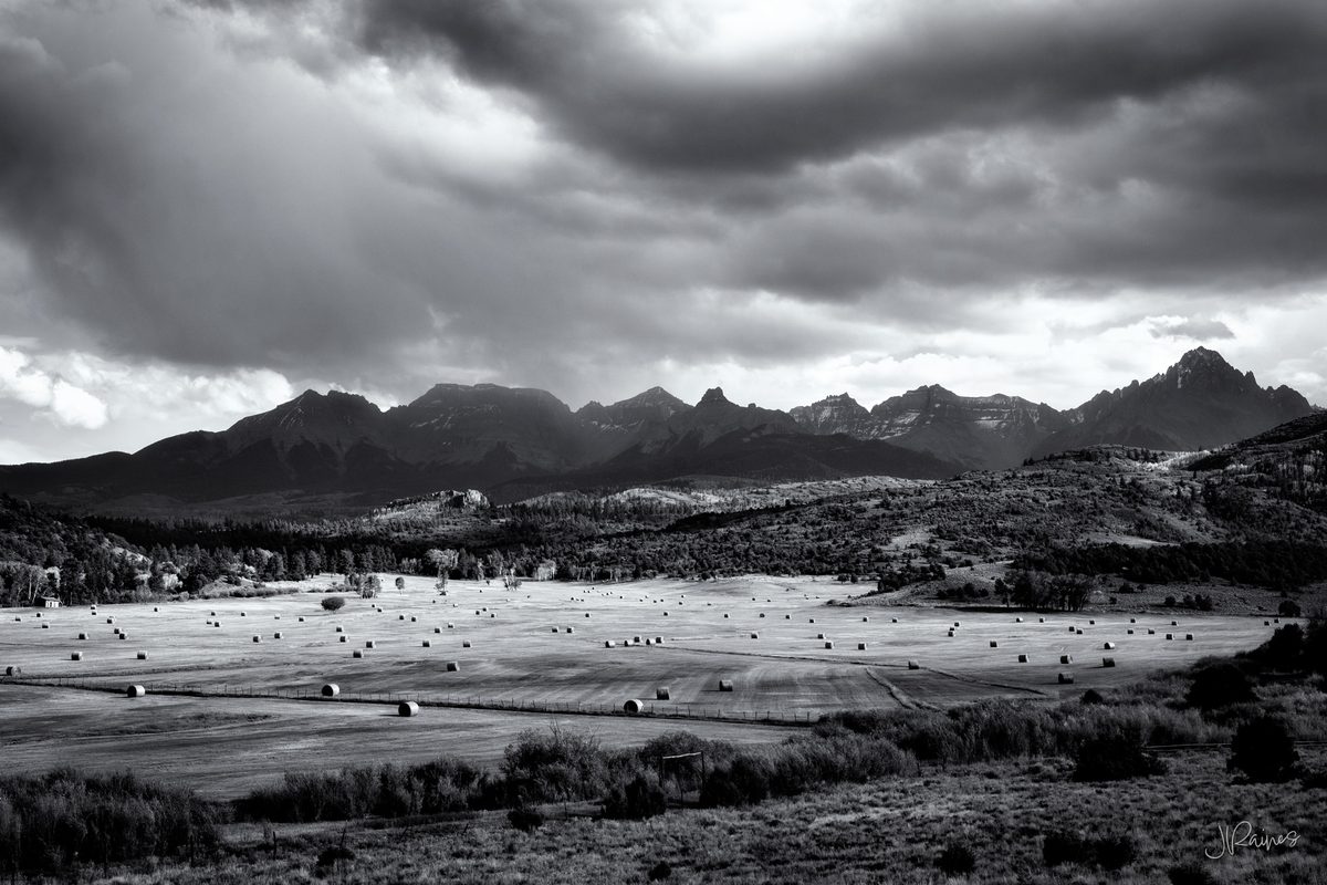 Hay bales scattered across a ranch field below the Sneffels Range under storm cloud, Ridgway, Colorado