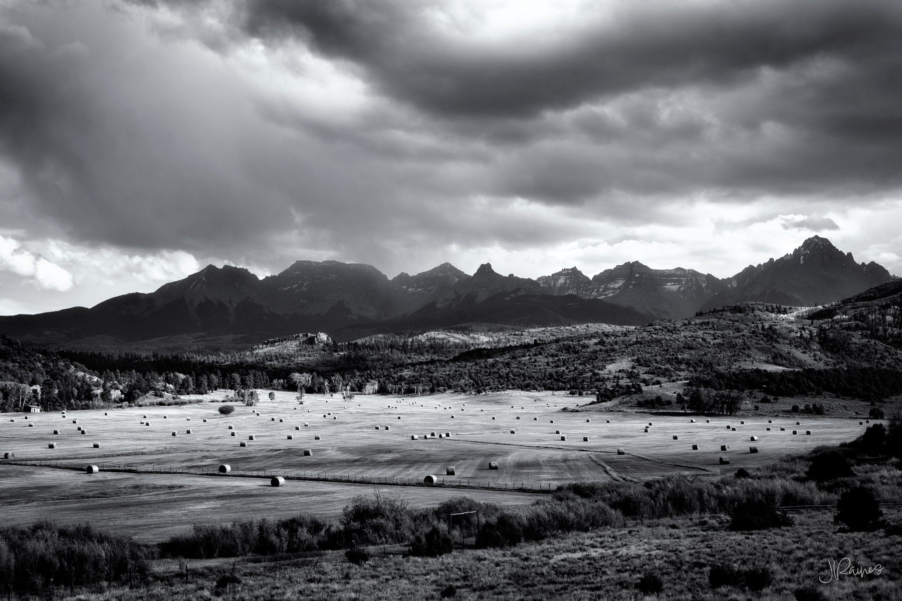 Hay bales scattered across a ranch field below the Sneffels Range under storm cloud, Ridgway, Colorado
