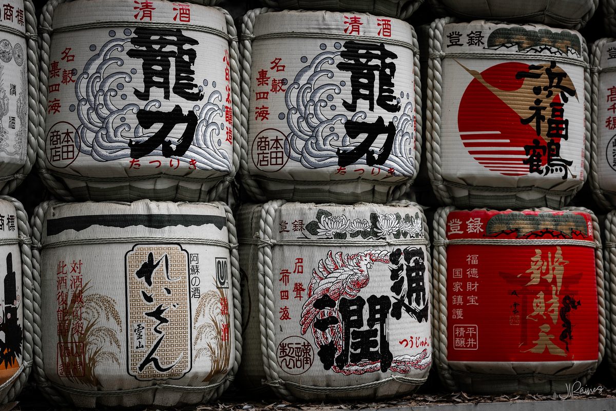 Sake barrels stacked and displayed in Japan — offerings donated to a shrine, each barrel painted with the brewery that gave it