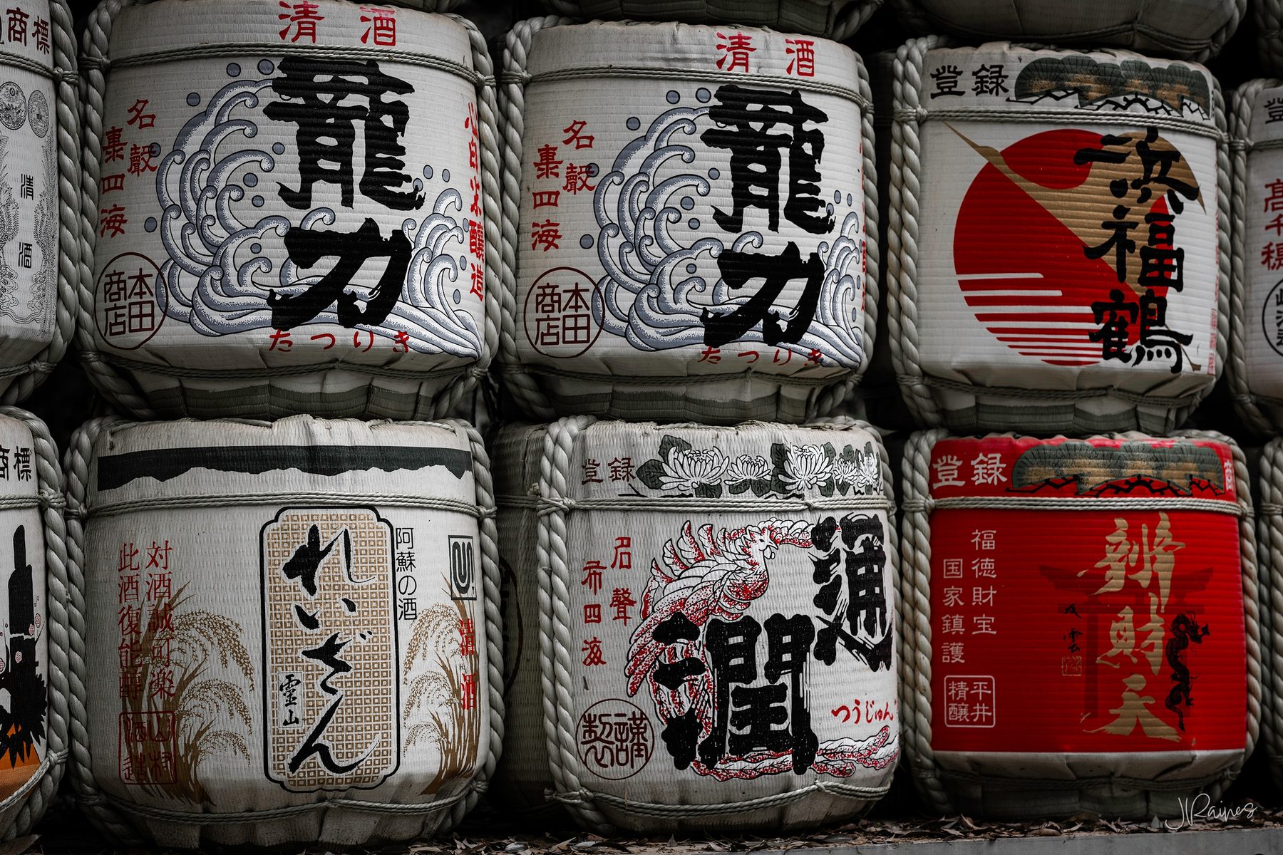Sake barrels stacked and displayed in Japan — offerings donated to a shrine, each barrel painted with the brewery that gave it