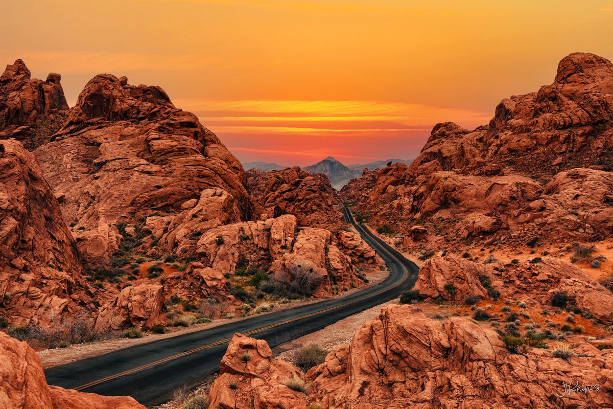 A road through old sandstone formations and mountains in the distance at sunset, Valley of Fire State Park, Nevada