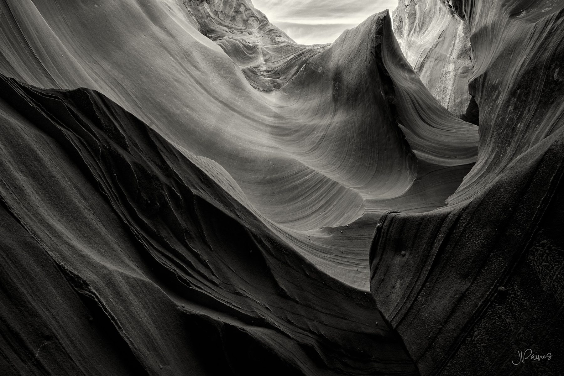 Near-monochrome slot canyon interior with a single glowing warm light source at a narrow opening, dark rock fin in the foreground, Page, Arizona