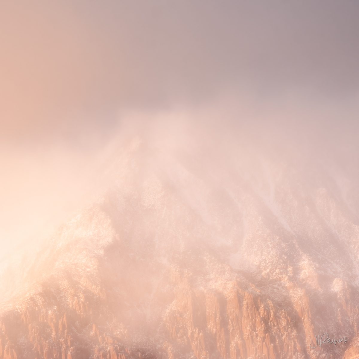 A mountain peak near Zion wrapped in snow cloud and mist, sunlit rose-gold rock below a vanishing cool blue-grey summit