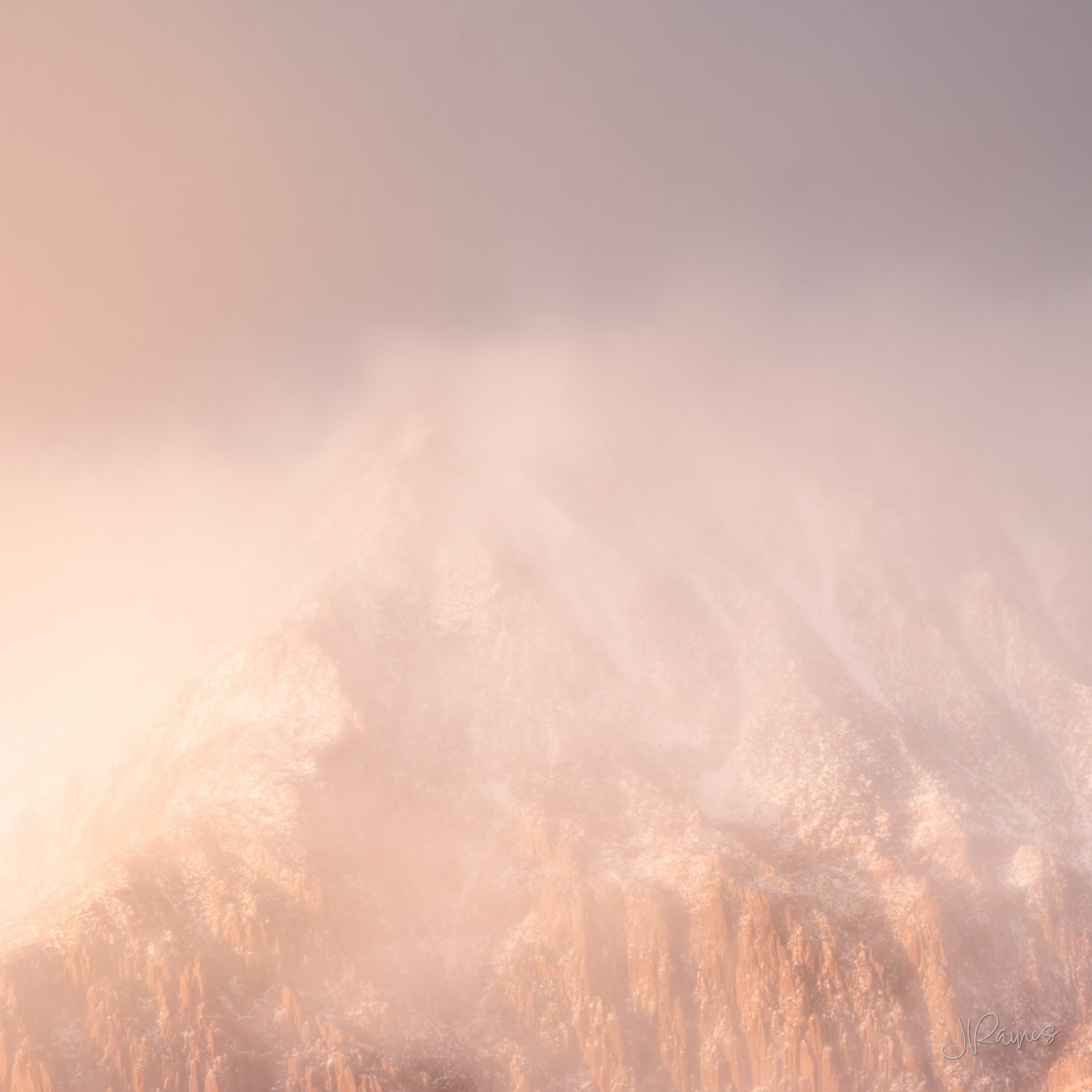 A mountain peak near Zion wrapped in snow cloud and mist, sunlit rose-gold rock below a vanishing cool blue-grey summit