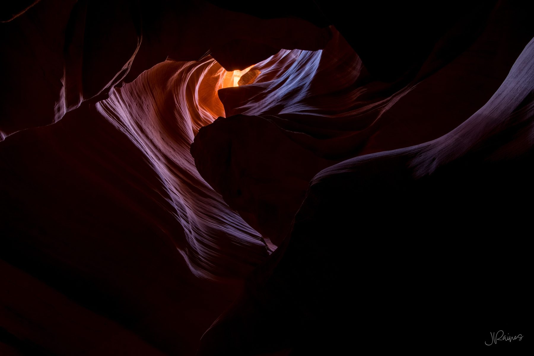 A heart-shaped slot canyon opening with warm glowing light at the far end and cool blue-lavender walls in shadow, Page, Arizona